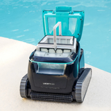 Front lifestyle view of the Maytronics Dolphin Liberty 600 robotic pool cleaner sitting poolside with its teal top lid open, showcasing the large top-access ultra-fine filter basket with carrying handle.
