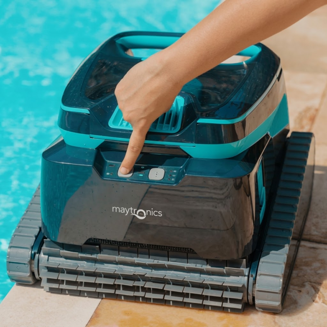 Close-up lifestyle view of a hand pressing the power button on the front control panel of the Maytronics Dolphin Liberty 600 robotic pool cleaner sitting poolside.