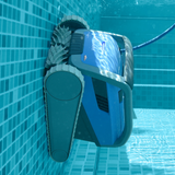 Underwater side view of the blue Maytronics Dolphin M 600 robotic pool cleaner climbing vertically up a tiled pool wall, showcasing its active scrubbing brushes and side track system.