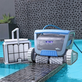 Poolside lifestyle view of the dark grey Maytronics Dolphin M 700 robotic pool cleaner resting on tiled pool coping next to its removed ultra-fine filter basket.
