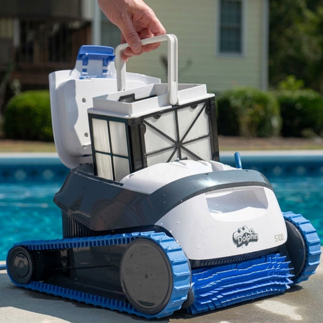 Outdoor lifestyle view of a hand removing the top-access fine filter basket from the white and grey Maytronics Dolphin S 100 robotic pool cleaner resting on poolside coping.