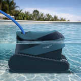 Split-level water line lifestyle view of the Maytronics Dolphin S1000 robotic pool cleaner partially submerged in a pool, showcasing its slate blue upper casing, dark grey body, continuous track belt, Maytronics branding, and attached blue power cable extending above the water surface.
