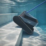 Side angle underwater lifestyle view of the Maytronics Dolphin S2000 robotic pool cleaner ascending tiled pool steps, highlighting its continuous rubber track, slate blue top housing with Maytronics branding, and blue power cable.