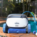 Outdoor lifestyle front view of the white and dark grey Maytronics Dolphin S 250 robotic pool cleaner resting on brick pool coping, showing its blue front active brush, blue continuous tracks, and floating cable.