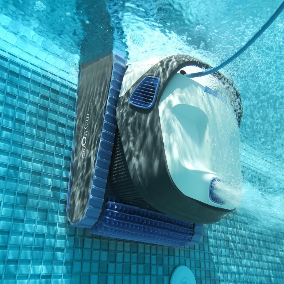 Underwater action view of the white and dark grey Maytronics Dolphin S 250 robotic pool cleaner climbing a blue tiled pool wall while operating its PowerStream mobility jet propulsion.