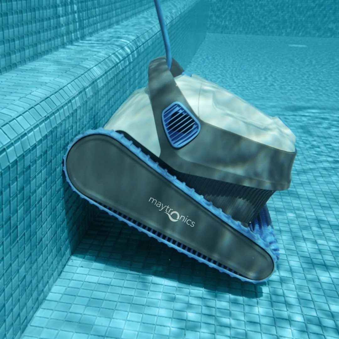 Underwater side view of the white and dark grey Maytronics Dolphin S 250 robotic pool cleaner climbing and cleaning pool steps lined with blue mosaic tiles.