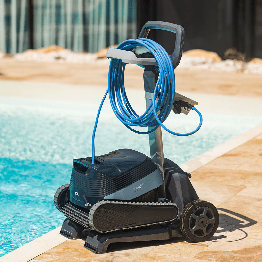 Outdoor lifestyle view of the Maytronics Dolphin S3000 robotic pool cleaner mounted on its premium transport caddy by the poolside, showing the coiled blue power cable neatly wrapped on the caddy hook and power supply unit.