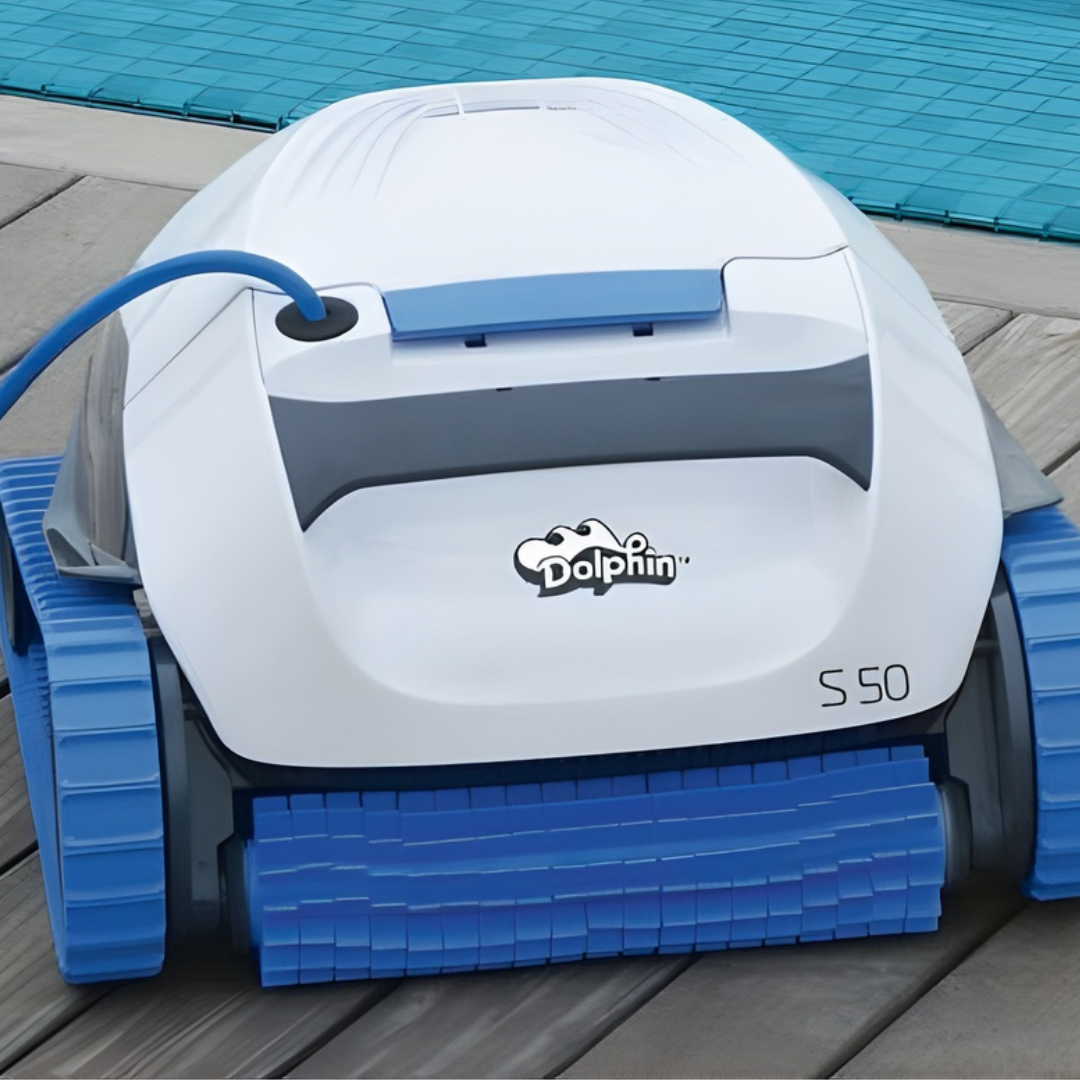 Front close-up view of the white and light blue Maytronics Dolphin S 50 robotic pool cleaner resting on wooden decking next to a pool, showcasing its blue front scrubbing brush and continuous tracks.