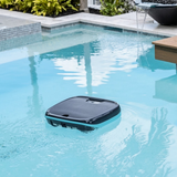 Outdoor lifestyle view of the Maytronics Dolphin Skimmi 200 robotic pool skimmer actively floating and operating on clear pool water in a backyard swimming pool setup with a stone water feature.