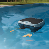 A grey Maytronics Dolphin Skimmi solar pool skimmer robot cruising on blue water toward floating leaves.