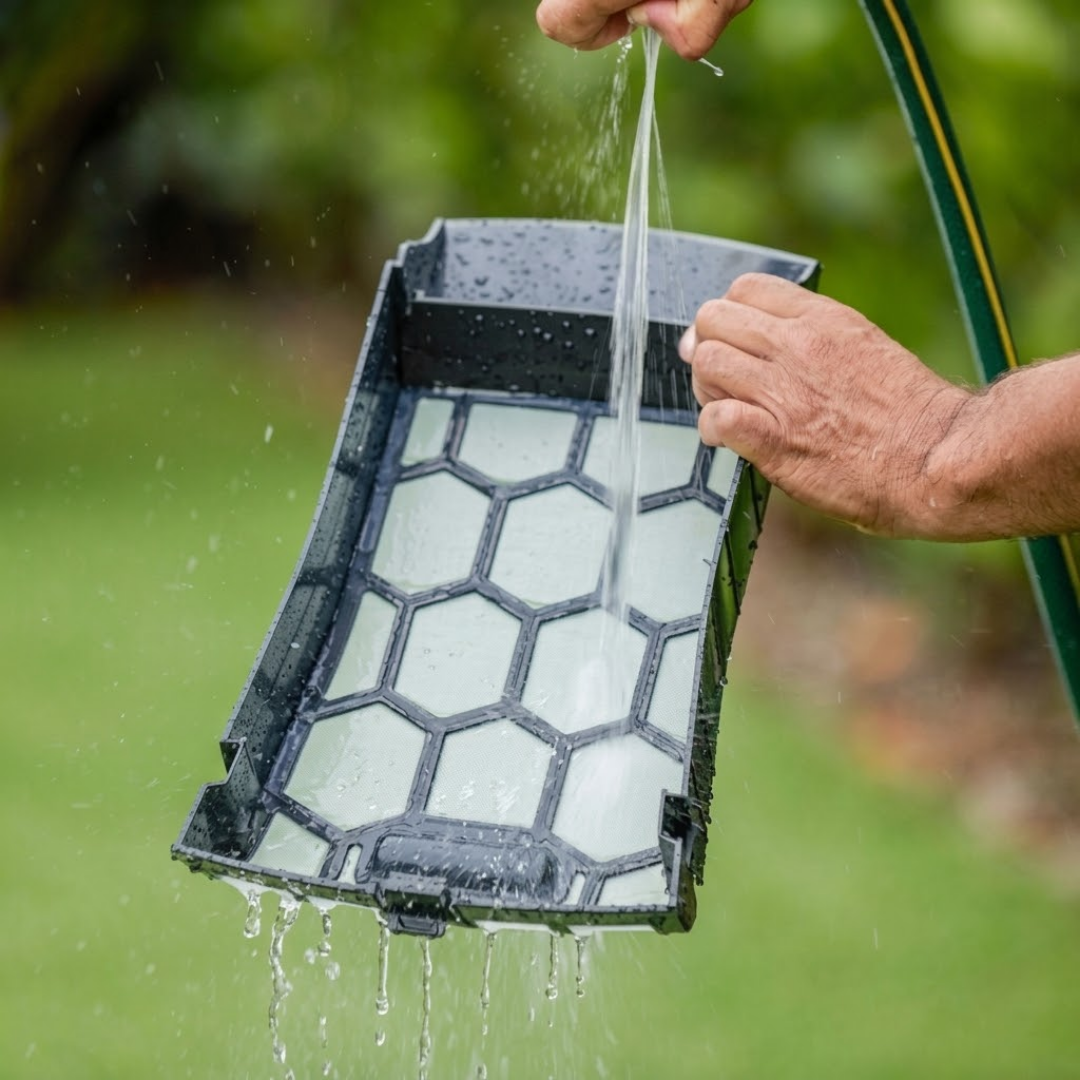 Close-up outdoor lifestyle image of a person rinsing out the removable fine mesh filter basket of a Maytronics Dolphin Skimmi robotic pool skimmer using a garden hose.