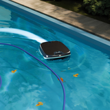 An overhead view of a Maytronics Dolphin Skimmi solar pool robot navigating clear blue water to skim floating autumn leaves