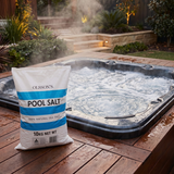A 10kg bag of Olsson's 100% Natural Sea Salt sitting on a timber deck next to a steaming outdoor hot tub spa with bubbling water.