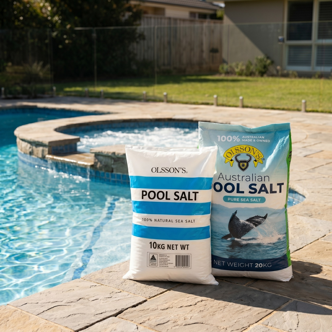 Two bags of Olsson's Australian Pool Salt (10kg and 20kg) sitting on a stone patio next to a clear blue swimming pool and backyard spa.