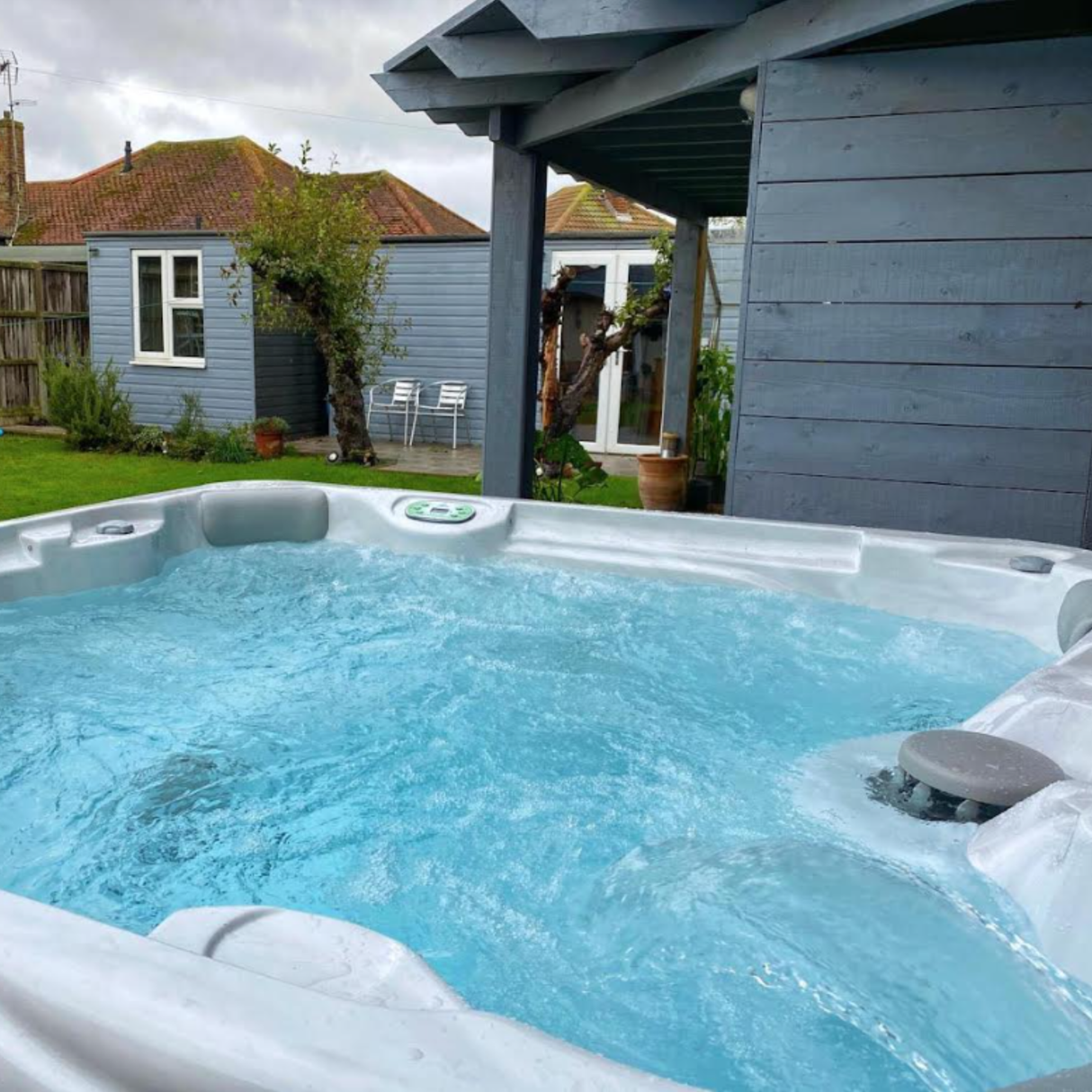 Outdoor backyard spa with bubbling blue water highlighting an installed grey CMP filter safety vane weir cap next to a grey wooden cabin building.