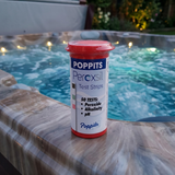A bottle of Poppits Peroxsil Test Strips on a marbled spa edge at night, showing 50-count capacity for peroxide, alkalinity, and pH testing in a lit hot tub.