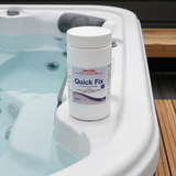 A 1kg white container of Poppits Quick Fix chlorine-free spa oxidiser resting on the white molded shell corner of an outdoor hot tub pool.