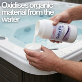 A person pouring Poppits Quick Fix chlorine-free spa oxidiser into a white cap over a backyard hot tub, with text overlay stating that it oxidises organic material from the water.