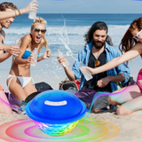 portable Bluetooth speaker playing music on a sandy beach for a group of friends celebrating in swimsuits near ocean waves.