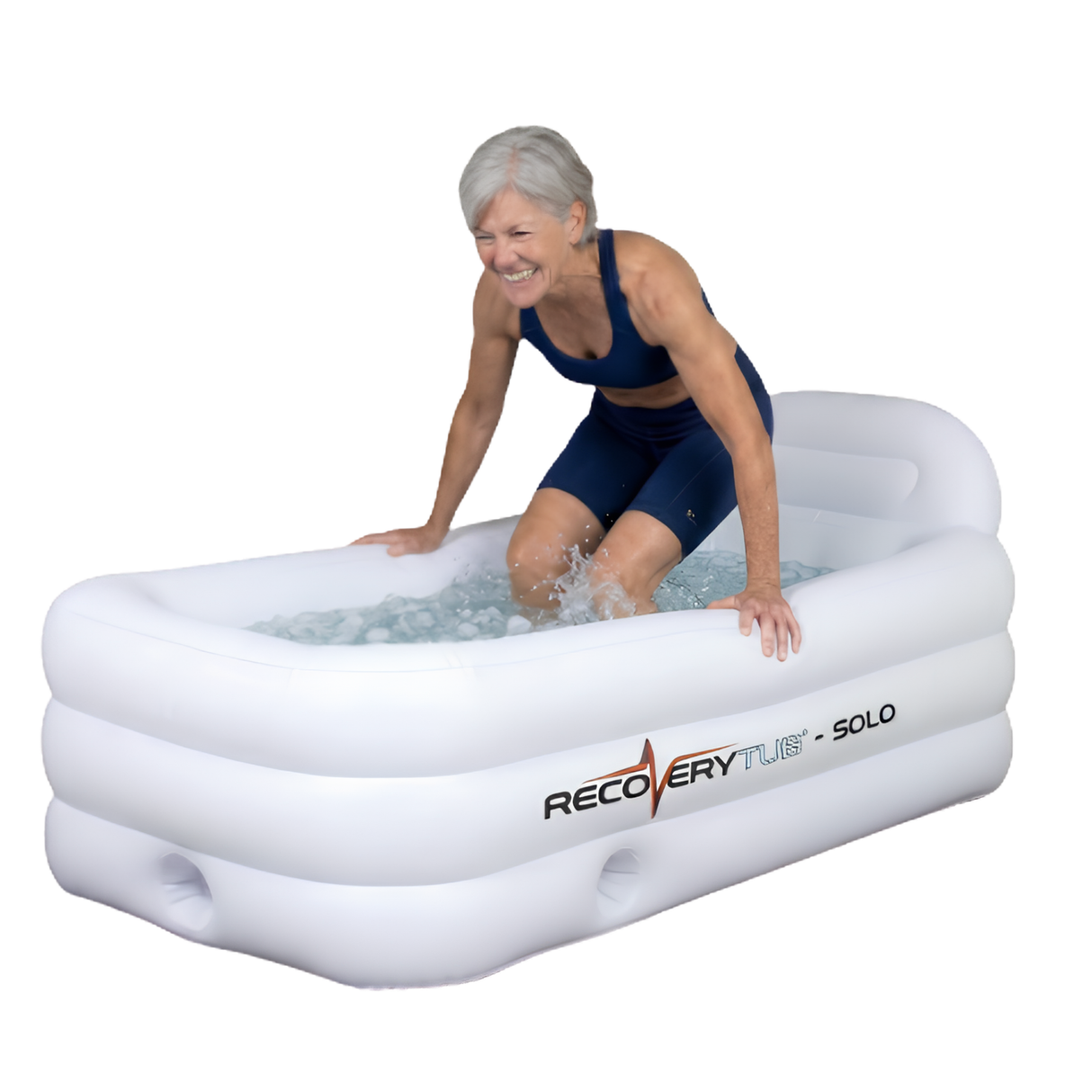 A smiling senior female athlete in athletic wear stepping out of a white rectangular RecoveryTub Solo inflatable ice bath filled with ice water, isolated on a white background.
