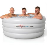 Three smiling male athletes sitting inside a large white inflatable RecoveryTub Team ice bath packed with ice cubes, showing the spacious capacity for group athletic cold therapy recovery against a clean white background.