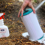A person using a garden hose to rinse a pleated spa cartridge filter after applying BioGuard SPA Filter Renew. The foaming action shows the cleaner lifting dirt, oils, and scale from the filter pleats during a deep clean.