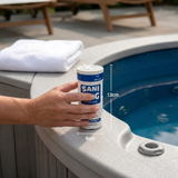 Hand holding a Sani-King Adjust-A-Flo spa dispenser next to a hot tub, with graphic lines showing its 13cm height and 6cm width dimensions.