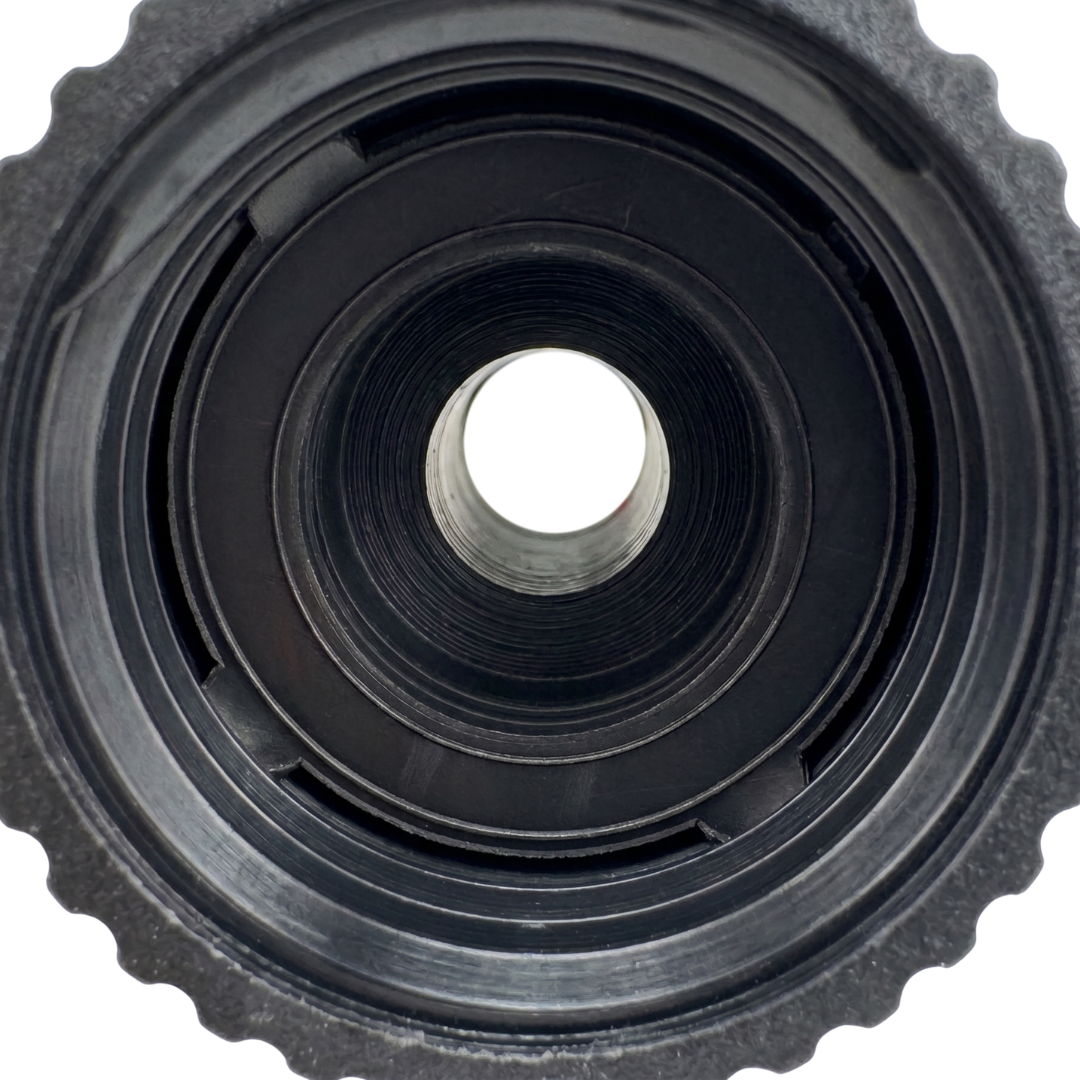 Direct overhead view looking straight through the concentric circular chambers and internal threads of a black plastic spa drain tap connector showing a clear center bore hole
