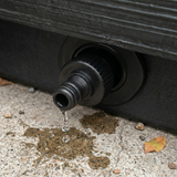 Close up view of a black plastic spa drain tap connector adapter installed into a hot tub lower cabinet panel with water dripping onto a concrete floor