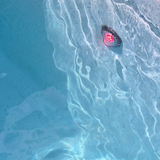 Overhead in-situ view of a Spa Electrics EMF Multi Plus LED pool light emitting red light underwater beneath gentle surface ripples in a light blue swimming pool.