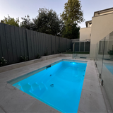 High-angle outdoor lifestyle shot of a modern backyard swimming pool illuminated in bright light blue by Spa Electrics EMF Multi Plus LED lights at dusk.