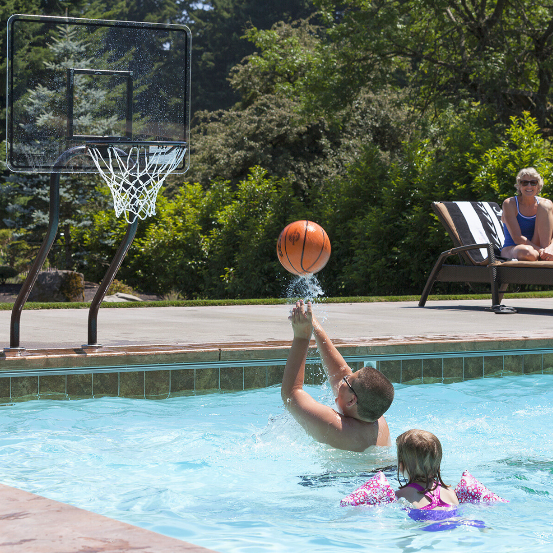 Children playing pool basketball with an S.R. Smith Challenge swimming pool basketball hoop system in a backyard