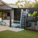 S.R.Smith Helix2 grey spiral pool slide ladder installation behind a modern black batten safety fence and glass pool fencing in a contemporary backyard.