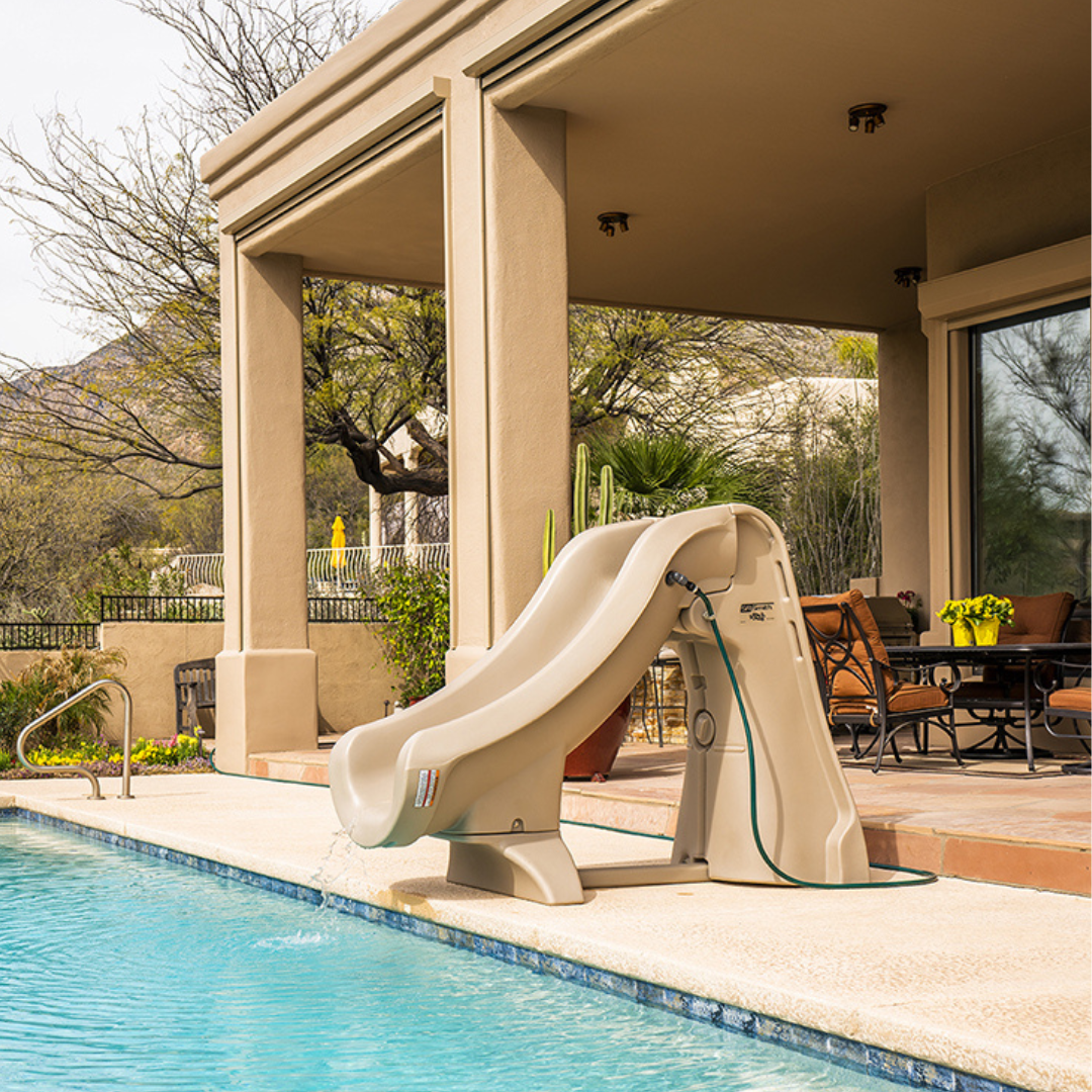 S.R.Smith SlideAway taupe removable water slide with attached garden hose running into an inground backyard swimming pool next to a covered outdoor patio dining area.