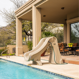 S.R.Smith SlideAway taupe removable water slide with attached garden hose running into an inground backyard swimming pool next to a covered outdoor patio dining area.