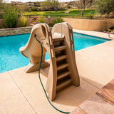 An adult using a rolling dolly cart to transport a compact taupe S.R.Smith SlideAway removable pool slide across a concrete backyard patio patio.