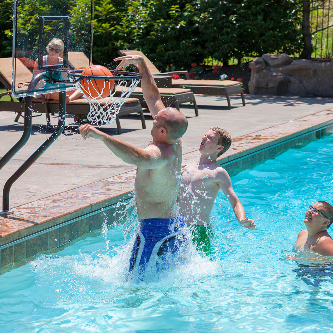  A man dunks a basketball into an S.R. Smith Swim-N-Dunk pool basketball hoop during a family game in an inground swimming pool.