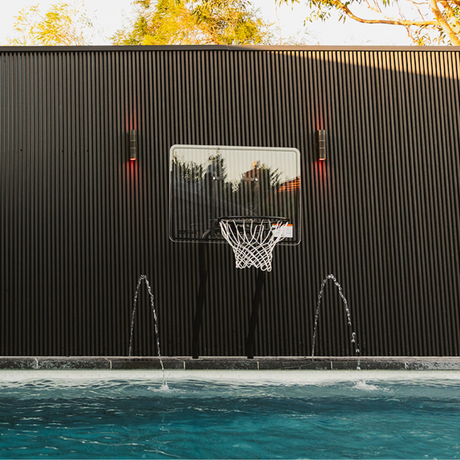 S.R. Smith Swim-N-Dunk pool basketball hoop installed poolside against a modern black slatted wall with water fountains