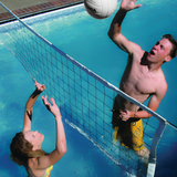 Action shot of a man spiking a water volleyball over an S.R. Smith Swim N' Spike net while a woman blocks the shot in a sunny swimming pool.