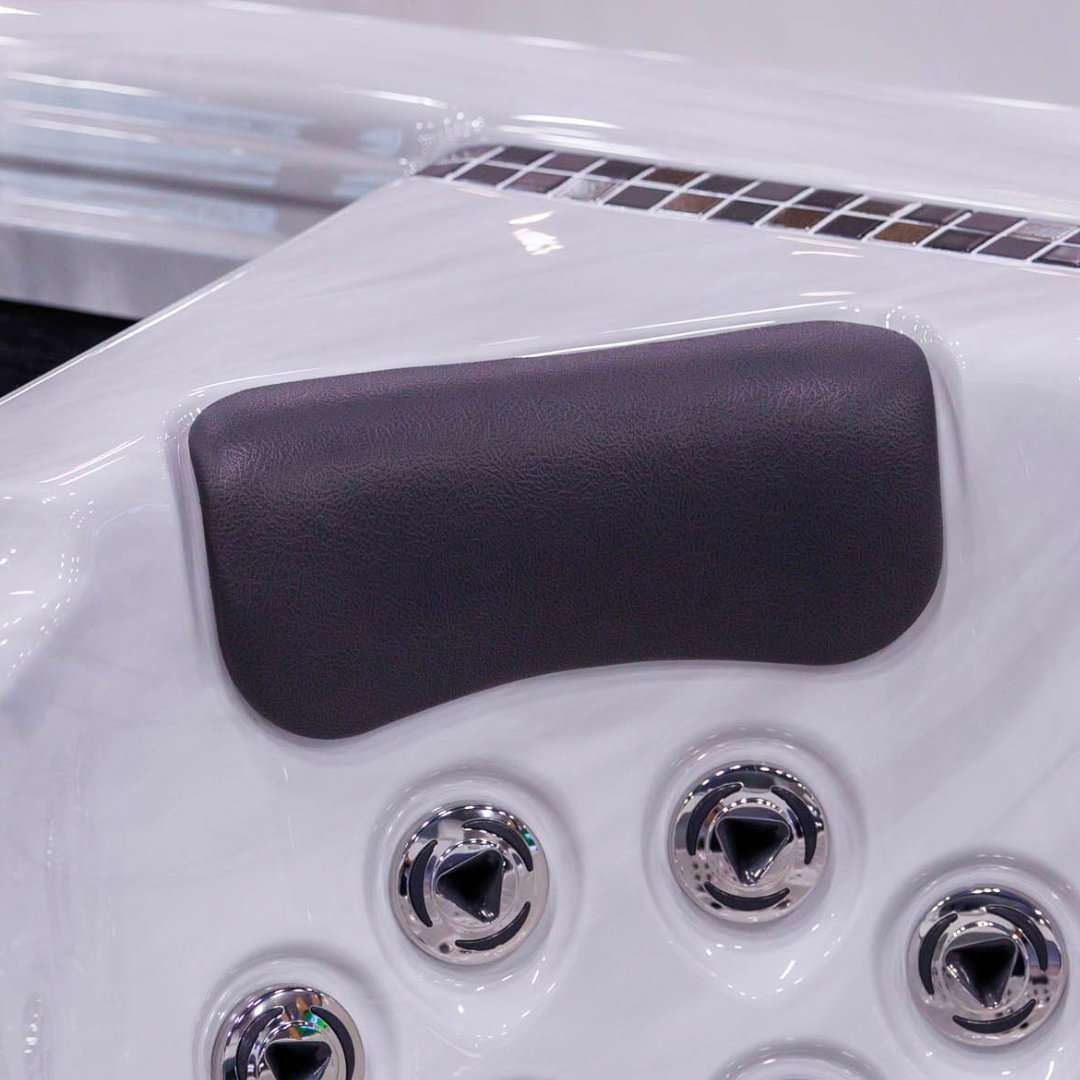 Close-up view of a Tropic Seas Spas Lounge series charcoal gray headrest pillow installed in a white acrylic hot tub seat directly above stainless steel hydrotherapy massage jets.