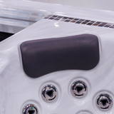 Close-up view of a Tropic Seas Spas Lounge series charcoal gray headrest pillow installed in a white acrylic hot tub seat directly above stainless steel hydrotherapy massage jets.