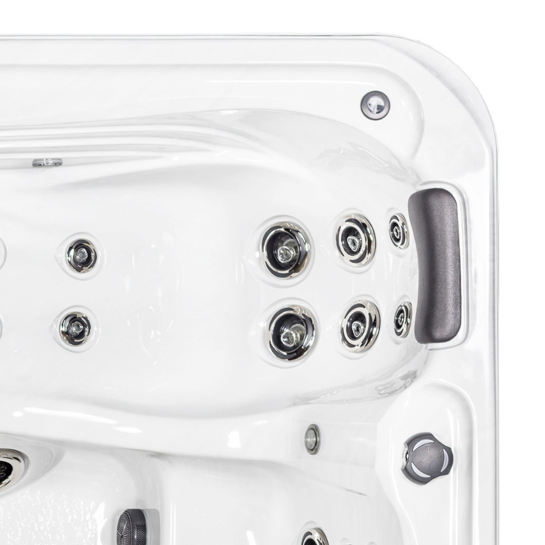 Overhead view of a Tropic Seas Spas Lounge series charcoal gray headrest pillow installed in the corner seat of a white acrylic hot tub, positioned next to a cluster of stainless steel hydrotherapy massage jets.