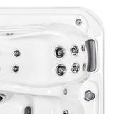 Overhead view of a Tropic Seas Spas Lounge series charcoal gray headrest pillow installed in the corner seat of a white acrylic hot tub, positioned next to a cluster of stainless steel hydrotherapy massage jets.