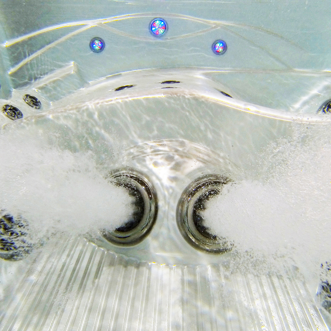 Underwater view of two Ultra Blaster 7 SS Graphite spa jets installed in a hot tub seat, actively spraying aerated streams of water into the pool.