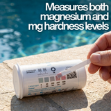 Close-up of a hand comparing a Zodiac MagnaPool test strip to the bottle chart with text: "Measures both magnesium and mg hardness levels," showing Calcium ppm and Hardness scales.