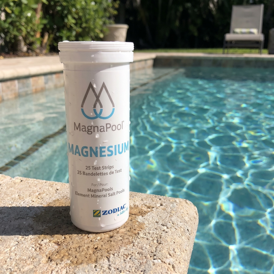 A bottle of Zodiac MagnaPool Magnesium Test Strips (25 count) sitting poolside on a stone ledge next to clear blue mineral pool water, used for measuring magnesium levels.