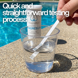 Close-up of a hand dipping a Zodiac MagnaPool Magnesium test strip into a clear water sample glass poolside, with text: "Quick and straightforward testing process."